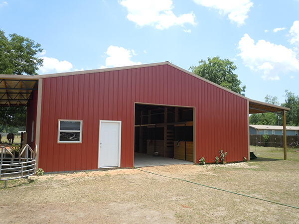 A metal building horse barn with a red metal roof and steel trusses.