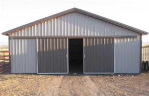 A Barndominium with a sliding metal door in the middle of a dirt field.