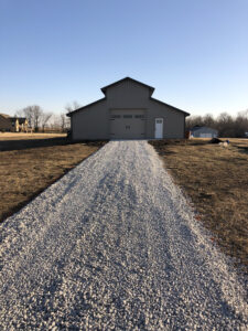 A gravel driveway leading to a metal barn.